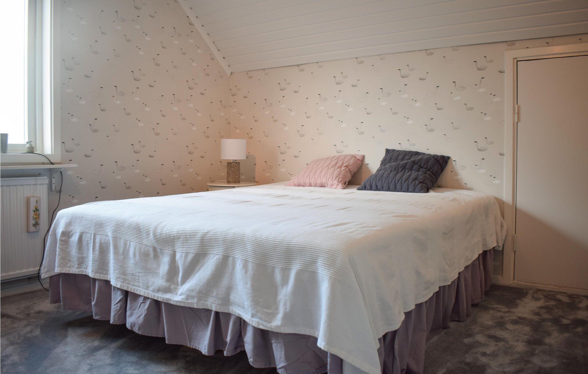 Un dormitorio con cama, mesita de noche, lámpara y ventana.