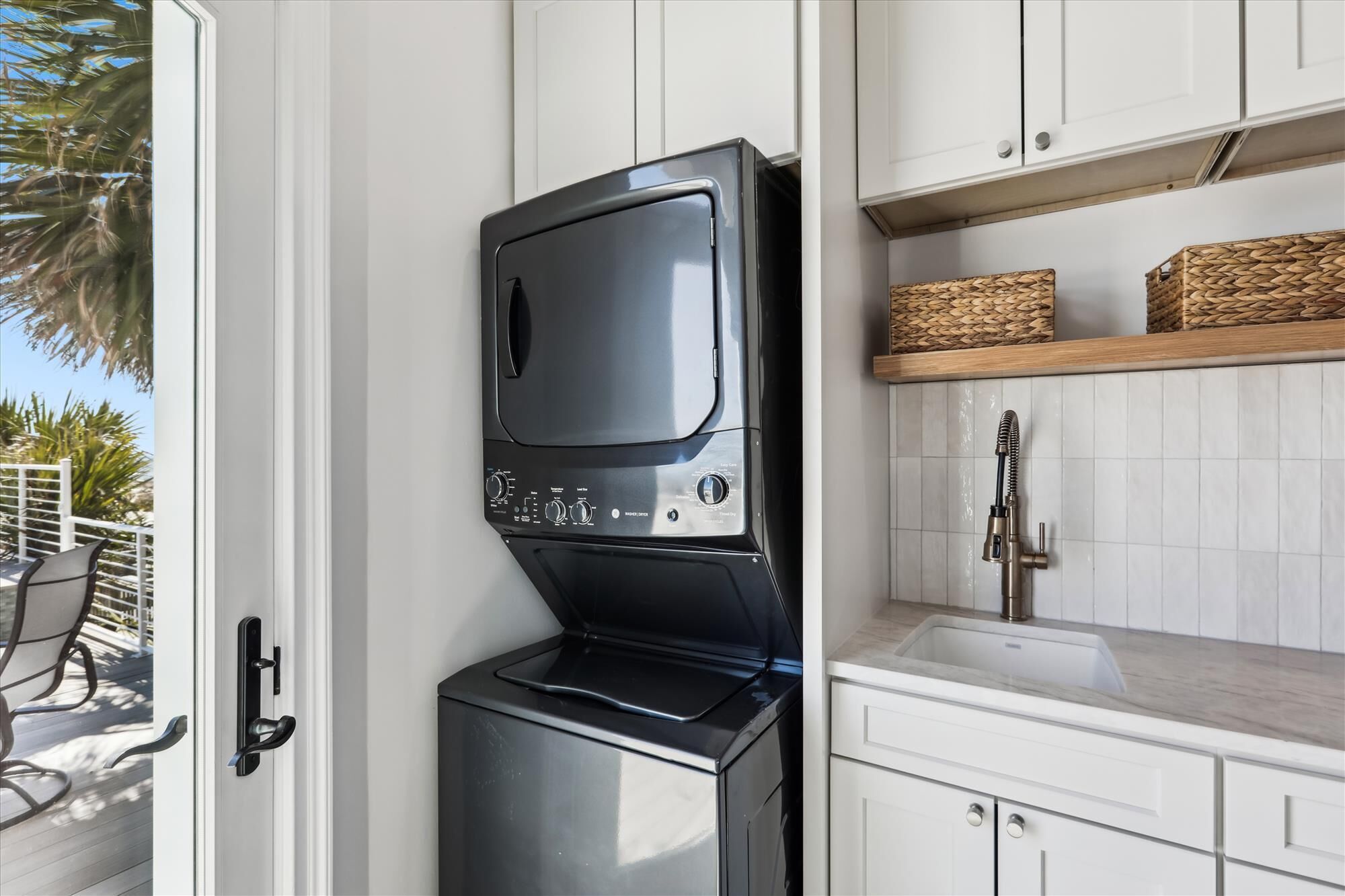 Una cocina compacta con microondas y horno integrados, muebles blancos, un lavamanos de acero inoxidable y un ventanal con vistas a una terraza.