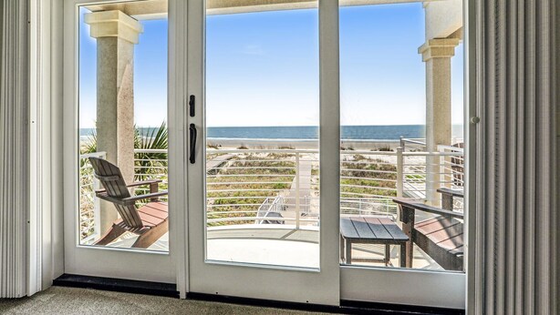 A room with a sliding glass door leading to an outdoor patio with a view of the beach.