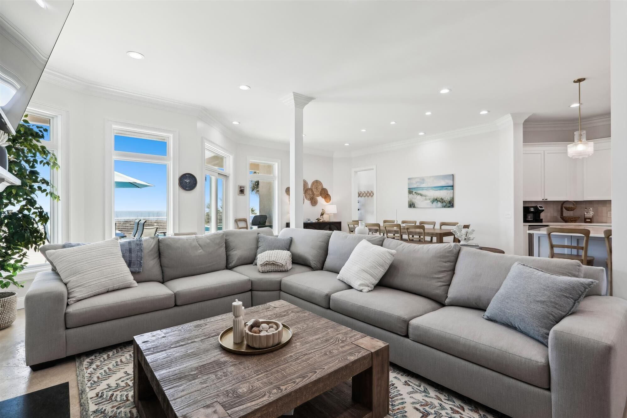 A modern living room with a large sectional sofa, a wooden coffee table, and a dining area with a view of the ocean.