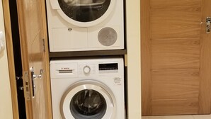 A laundry room with two stacked Bosch washing machines, a wooden cabinet above, and a wooden door to the right. - London Luxury 1 bed studio 5 mins from Ilford Stn free parking (London)