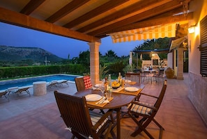 An outdoor dining area with a pool view, wooden pergola, and stone pillars.