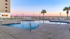 A swimming pool with lounge chairs and palm trees, surrounded by a low fence. - BEACHFRONT Ground Floor WALK-OUT 3Bdrm/2Ba Plantation Palms Great for Families (Gulf Shores)