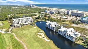 A golf course with a water feature, surrounded by hotel buildings and a beach in the background. - BEACHFRONT Ground Floor WALK-OUT 3Bdrm/2Ba Plantation Palms Great for Families (Gulf Shores)