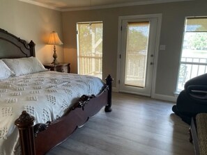 A bedroom with a large bed, a nightstand, a lamp, and a sliding glass door leading to a balcony. - Enchanting lake home with amazing views! Very Safe (Baton Rouge)
