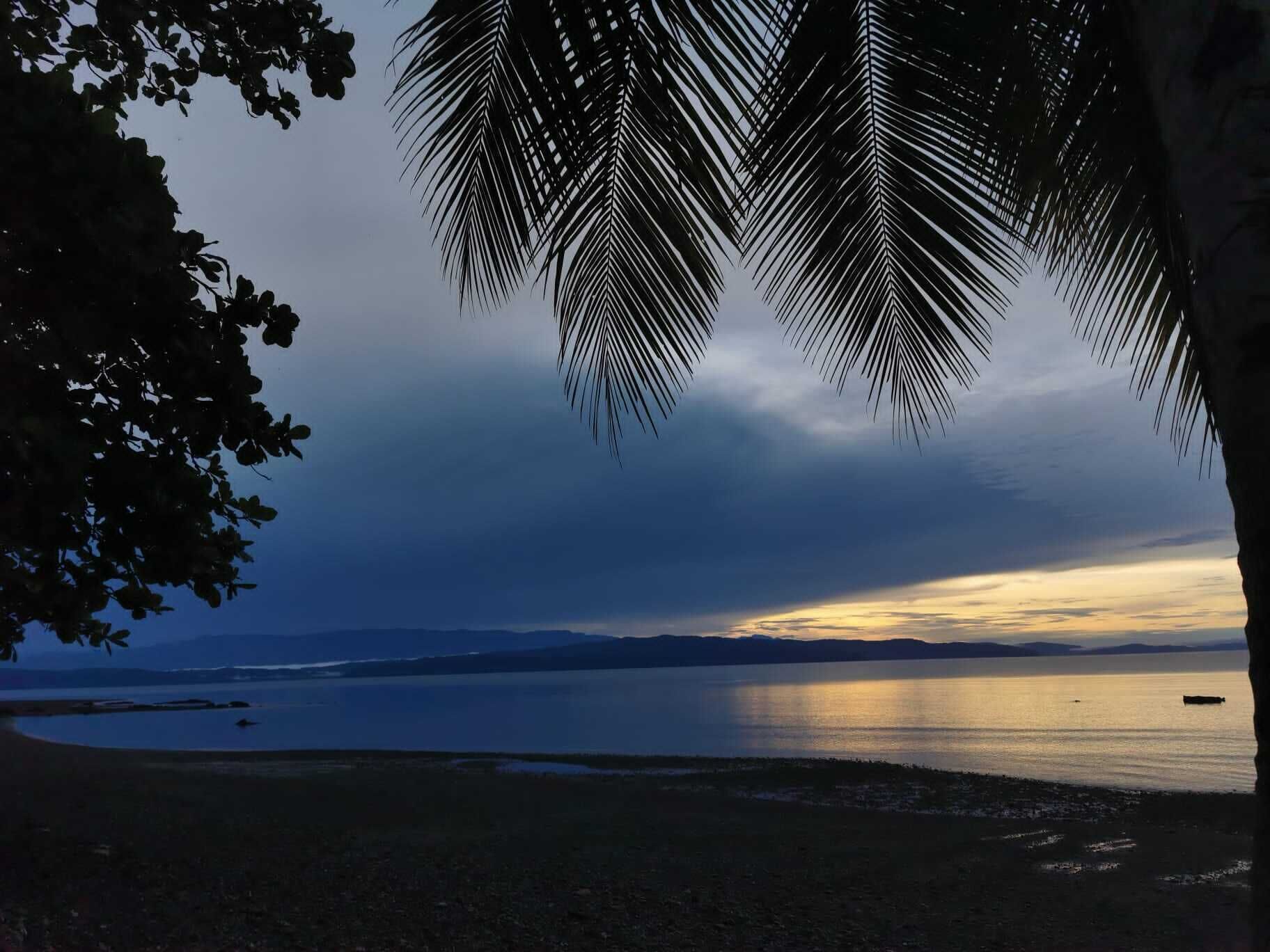 Une plage bordée d’une mer calme, un ciel dégagé et, au loin, la silhouette d’une chaîne de montagnes.