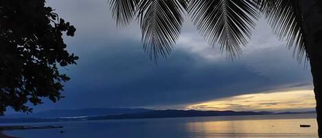 Une plage bordée d’une mer calme, un ciel dégagé et, au loin, la silhouette d’une chaîne de montagnes.