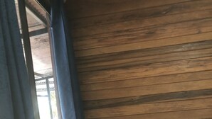 Een kamer met houten wanden, een raam met gordijnen en een houten plank met opgerolde handdoeken.