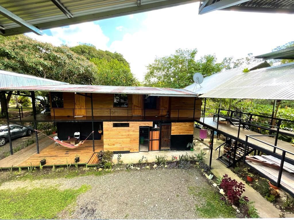 Une maison en bois à deux étages, dotée d’un porche couvert, d’un hamac et d’une antenne parabolique.