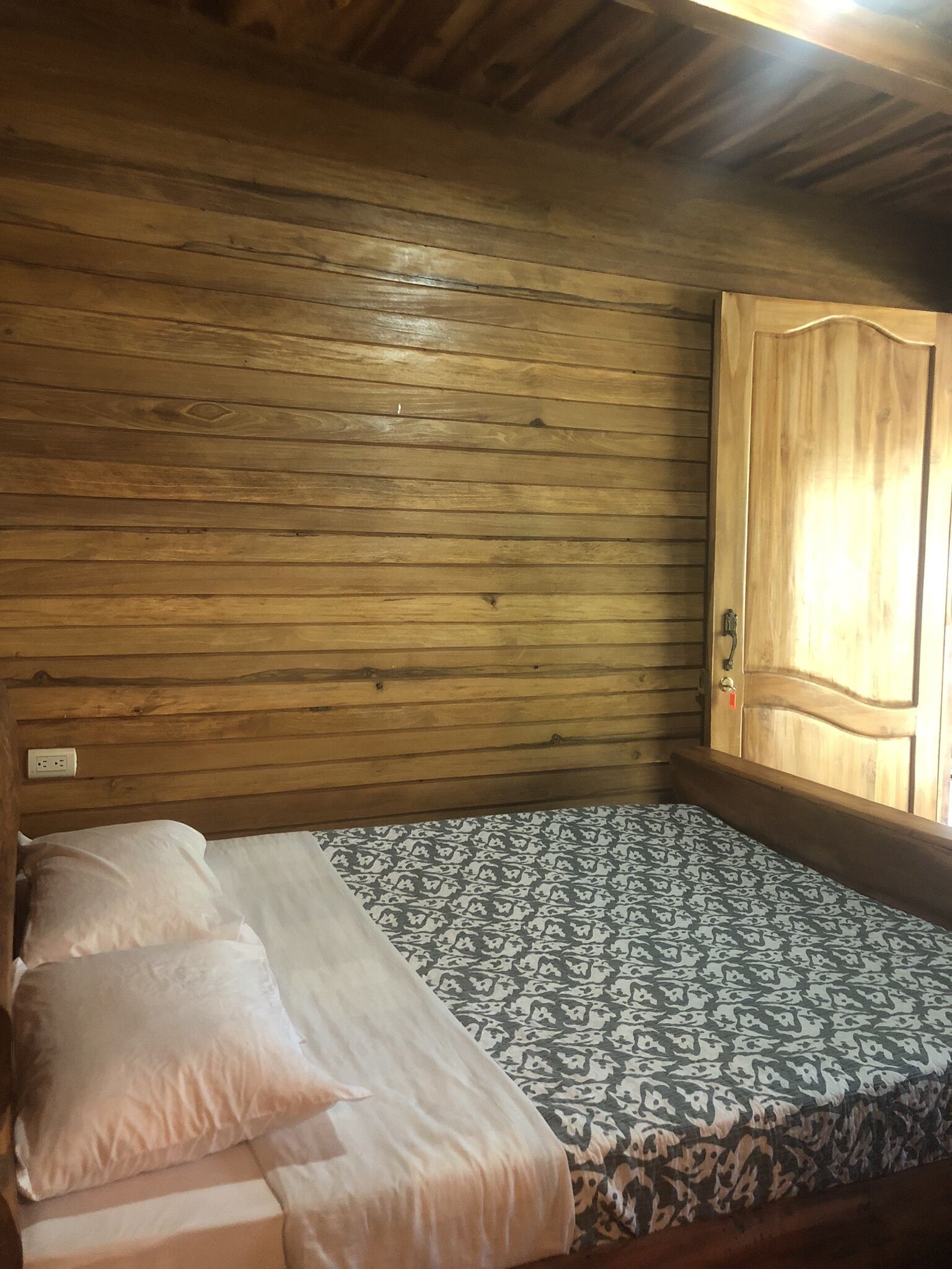 A wooden-paneled room with a bed, a patterned bedspread, and a wooden door.