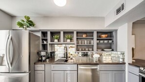 A modern kitchen with grey cabinetry, stainless steel appliances, and a central island. - Spacious 2BR condo with dual king suites, private patio, and access to resort-style pool and wellness amenities in Dallas’s coveted Lakewood neighborhood. (Dallas)