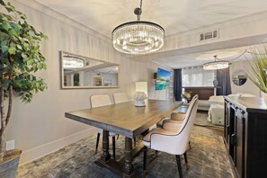 A dining area with a wooden table, white chairs, a chandelier, a large mirror, and a potted plant.
