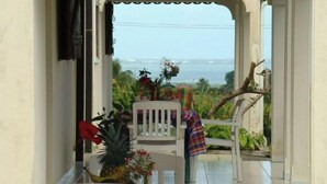 A dining area with a view of the ocean, featuring a table and chairs with a colorful tablecloth, a pineapple, and flowers. - Spacious T3 gîtes, lovely terrace and shared swimming pool, sea view, peaceful (Capesterre-Belle-Eau)