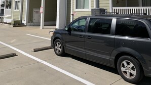 Un edificio de apartamentos de varios pisos con balcones, un estacionamiento y un vehículo estacionado al frente.