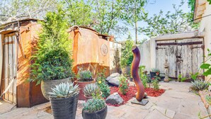 A garden with potted plants, a rustic metal structure, and a wooden door. - Adobe Studio: 2 Blocks to Dtwn Santa Fe Plaza! (Santa Fe)