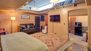 A cozy room with a bed, a leather sofa, a TV, and a bookshelf under a skylight. - Adobe Studio: 2 Blocks to Dtwn Santa Fe Plaza! (Santa Fe)