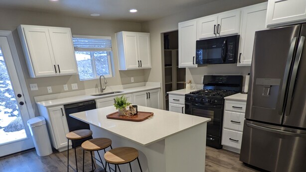A modern kitchen with white cabinets, a central island with stools, a stainless steel refrigerator, and a black stove.