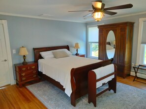 A bedroom with a wooden bed, nightstands, a dresser, a ceiling fan, and a large mirror.