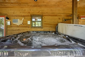 Interior de una cabaña de madera con un jacuzzi, paredes de madera, una bandera estadounidense enmarcada y una ventana con persianas.