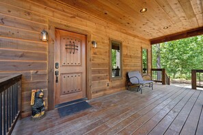 A wooden cabin with a front door, a bench, and a bear statue. - Waymaker, Couples, Hot Tub, Firepit, Soaker Tub (Broken Bow)