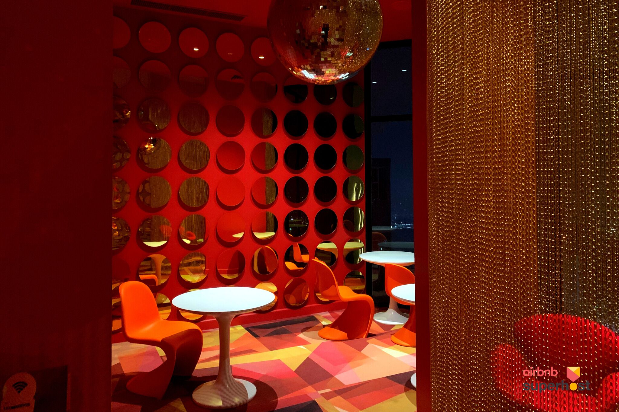 A vibrant room with a patterned wall, circular mirrors, and orange seating.