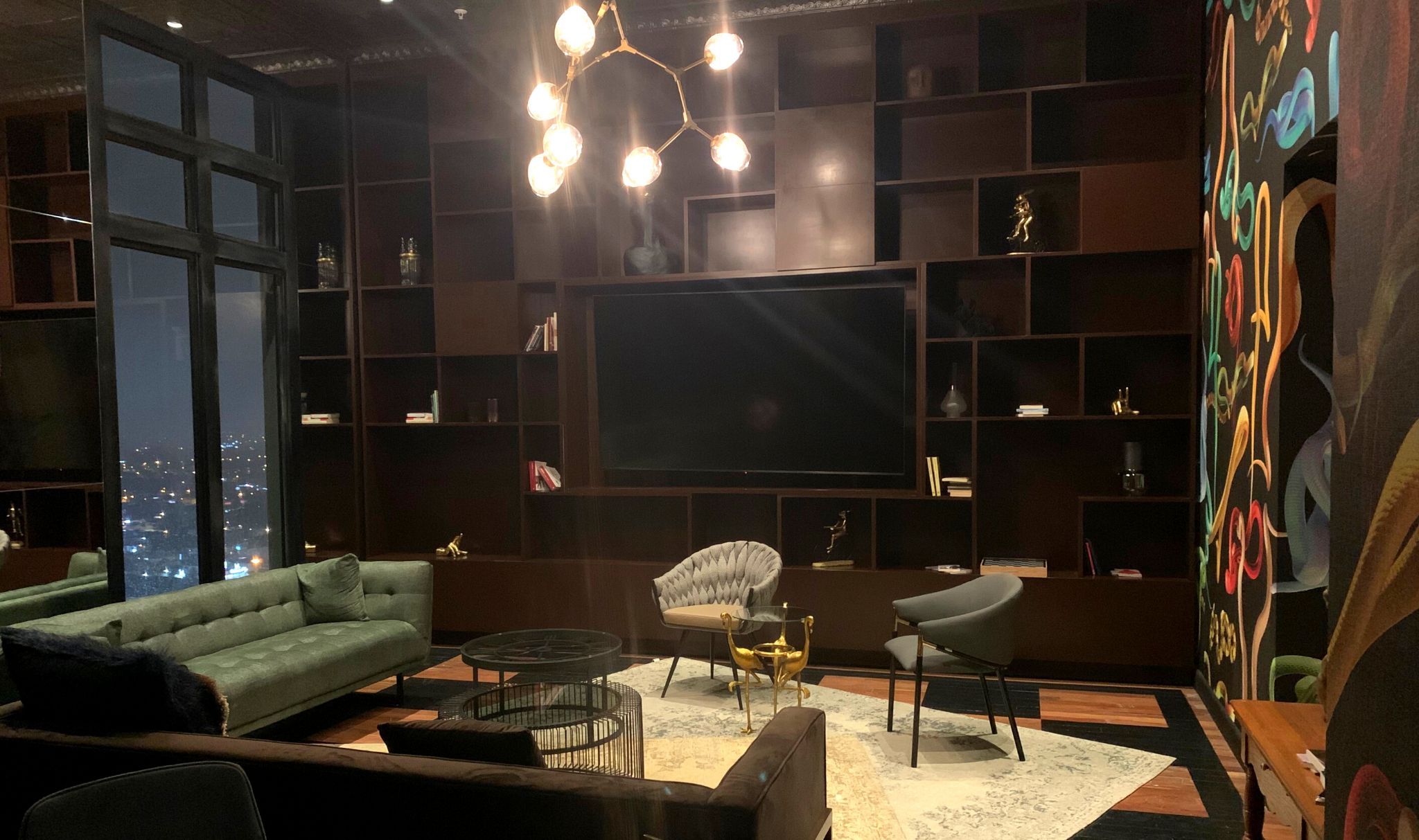 A modern living room with a large flat-screen TV, comfortable seating, and a city view.