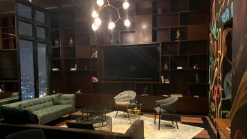 A modern living room with a large flat-screen TV, comfortable seating, and a city view.
