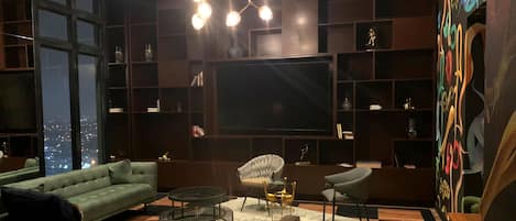 Una sala de estar moderna con un televisor de pantalla plana grande, asientos cómodos y vistas a la ciudad.