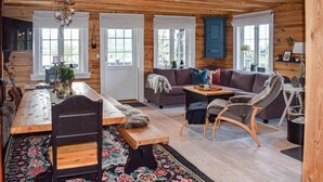 A cozy log cabin interior with a wooden dining table, a sofa, and a rocking chair.