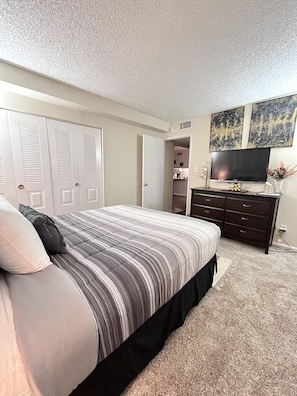 Un dormitorio con una cama, un aparador, un televisor y una puerta que da a otra habitación.
