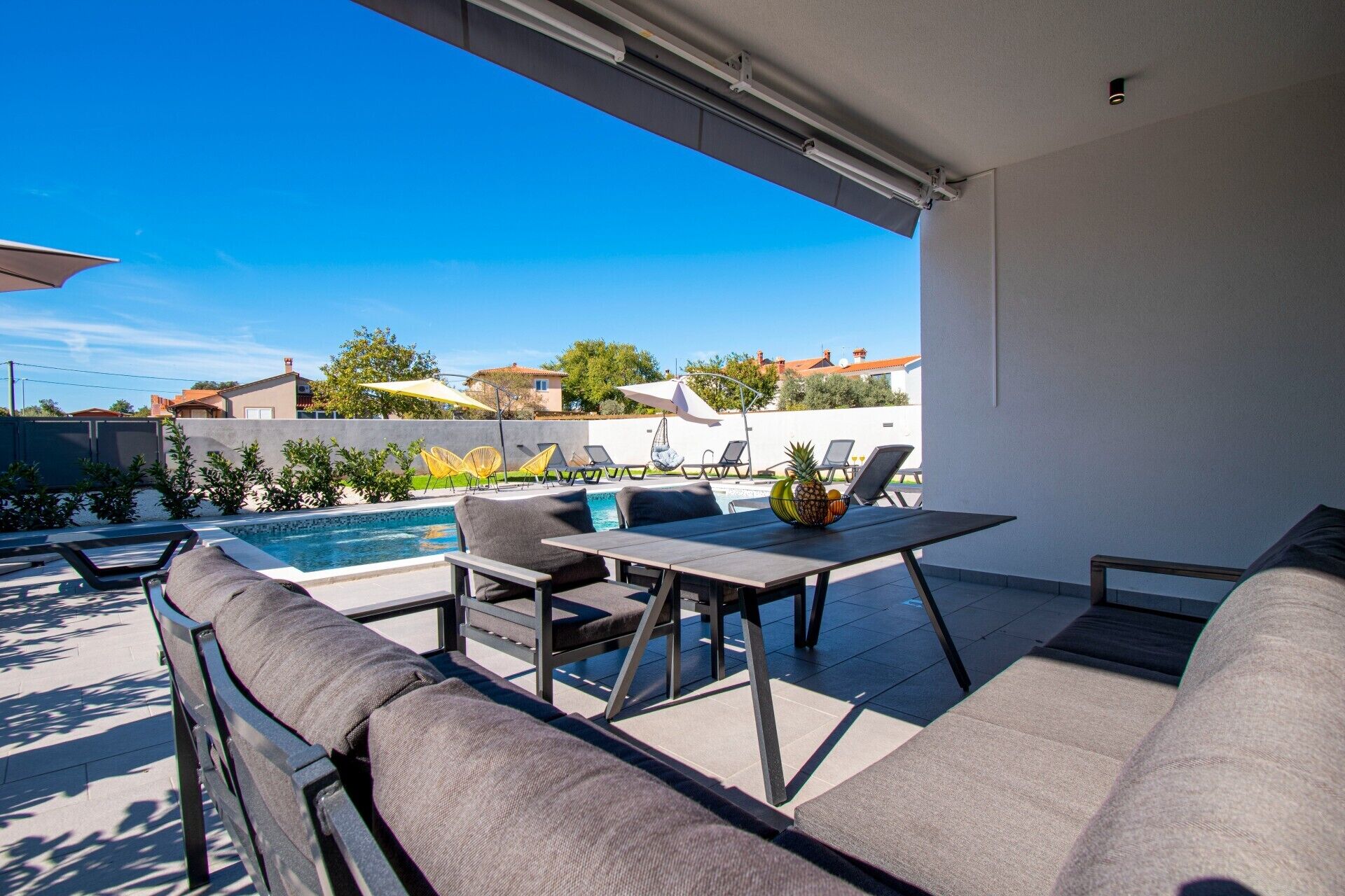 Une terrasse extérieure moderne avec une piscine, des chaises longues et une table garnie de fruits.
