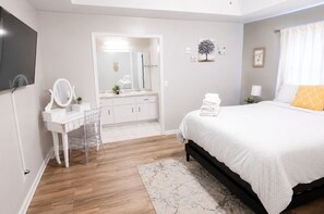 A bedroom with a bed, a bedside table, a mirror, a dresser, and a bathroom visible through an open door. - Spacious Home w/ Coffee Bar & GameRoom near Ft. Stewart & Savannah (Hinesville)