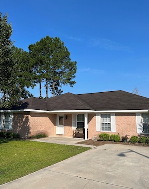 A single-story brick house with a front porch, a driveway, and a large tree in the background. - Spacious Home w/ Coffee Bar & GameRoom near Ft. Stewart & Savannah (Hinesville)
