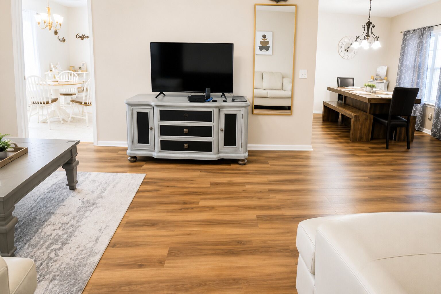 A living room with a flat-screen TV, a dining area with a wooden table, and a large mirror on the wall.