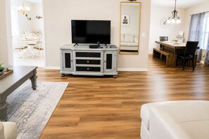 A living room with a flat-screen TV, a dining area with a wooden table, and a large mirror on the wall. - Spacious Home w/ Coffee Bar & GameRoom near Ft. Stewart & Savannah (Hinesville)