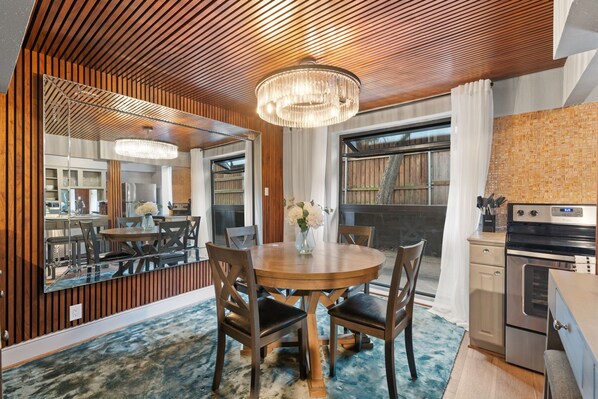 A modern dining area with a wooden ceiling, a chandelier, and a large mirror reflecting the room.