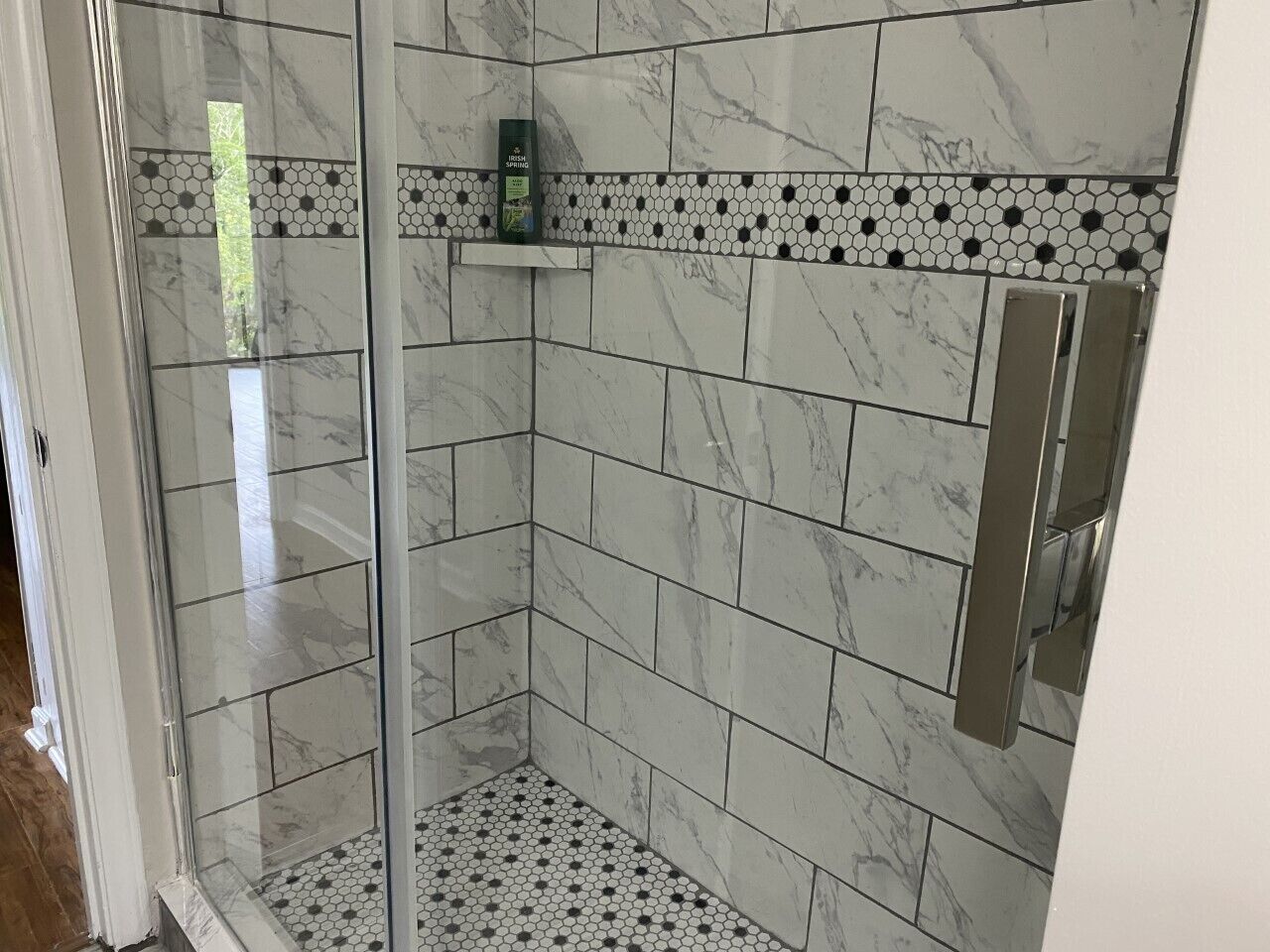 A shower with white marble tiles and a glass door.