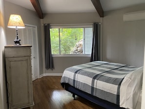 Un dormitorio con cama, mesita de noche, lámpara, ventana con cortinas y vistas a zonas verdes.