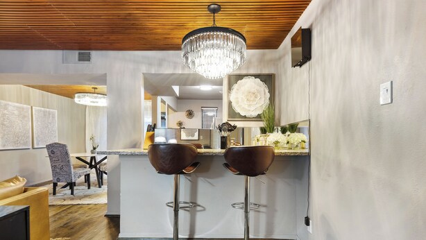 A modern kitchen with two bar stools, a chandelier, and a dining area with a wooden ceiling. - A bright two-bedroom condo with warm furnishings, neutral tones, and a comfortable living space overlooking the property’s resort-style surroundings. (Dallas)