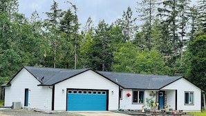 Un bâtiment blanc à deux étages, avec une porte de garage bleue, entouré d’une allée gravillonnée et d’une zone herbeuse.
