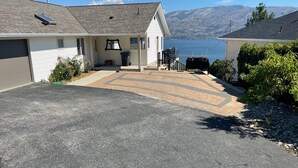 Una propiedad residencial con entrada pavimentada, un porche cubierto y vistas a un lago y montañas al fondo.