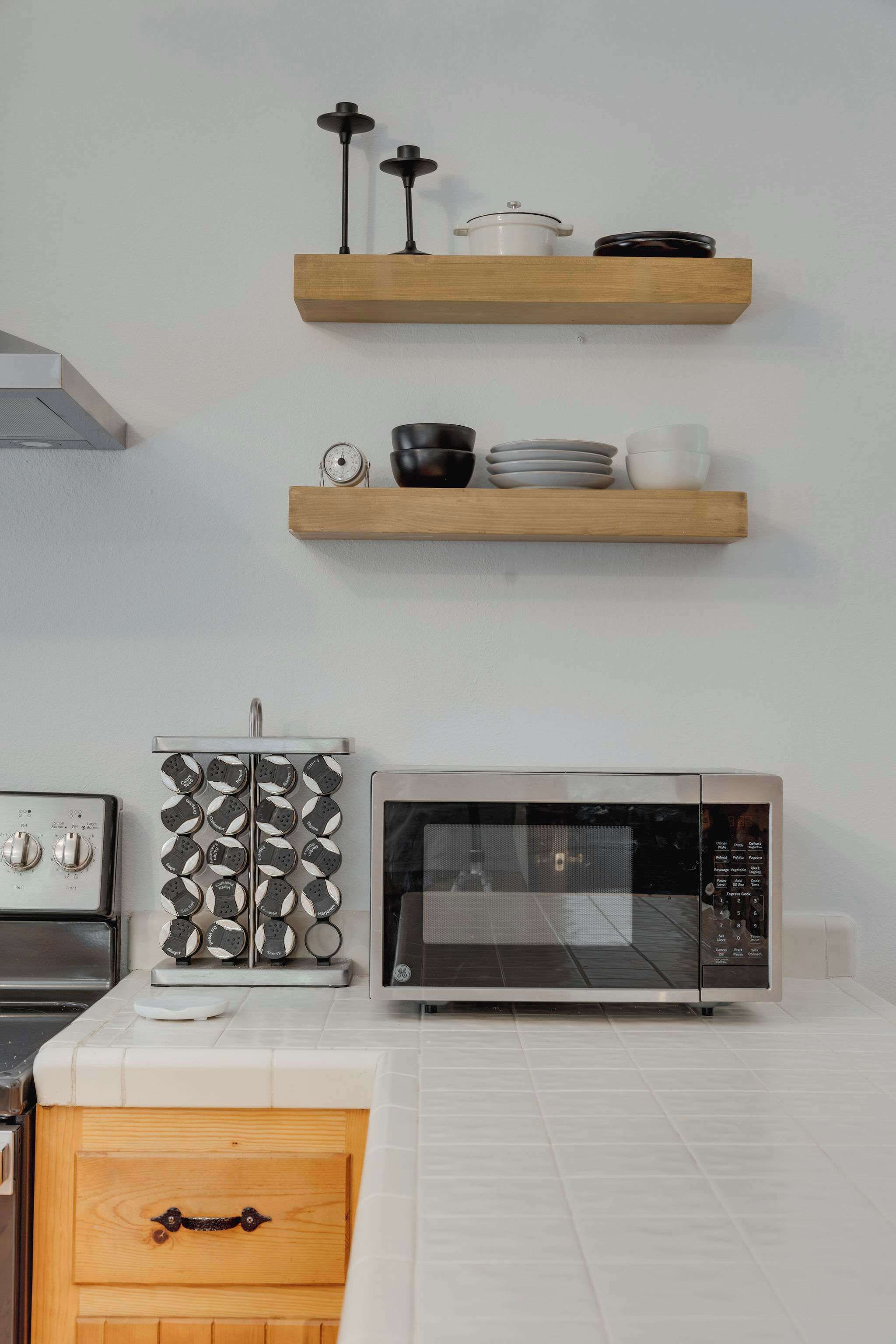 A kitchen with a microwave, a stove, and two wooden shelves above holding kitchenware.
