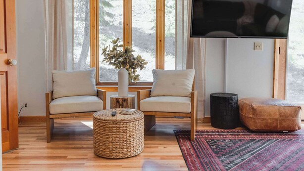 Ett mysigt vardagsrum med två fåtöljer, en tv, en växt och en flätad pall.