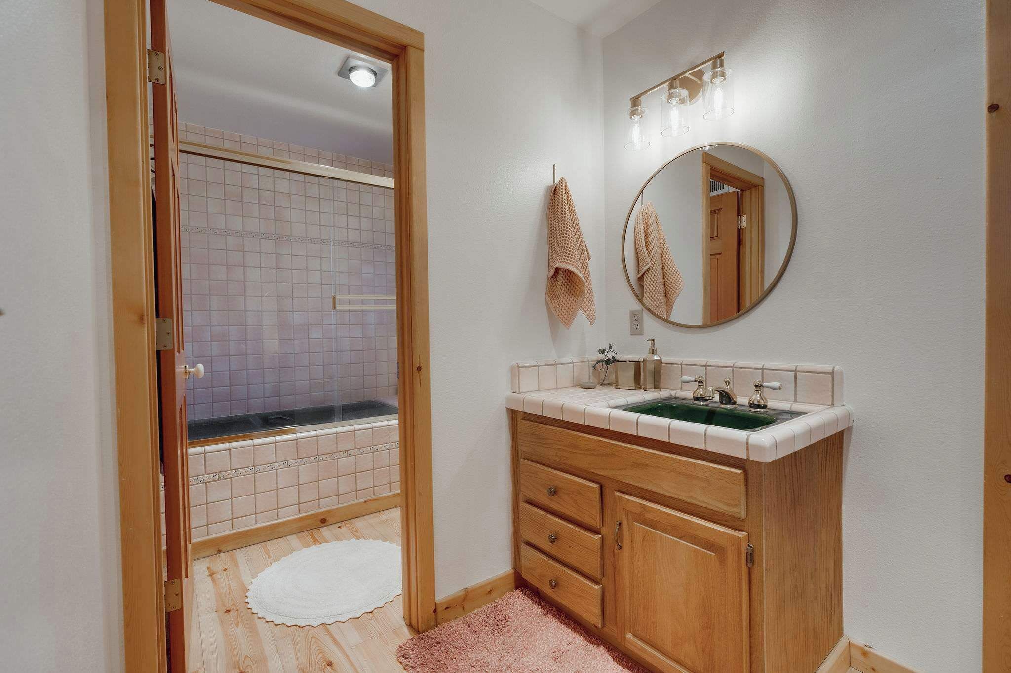A bathroom with a wooden vanity, a round mirror, and a tiled shower area.