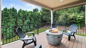 Una terraza techada con un brasero y sillas Adirondack, con vista a un bosque tupido.
