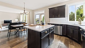 Una cocina moderna con armarios oscuros, una isla grande y un comedor con mesa y sillas de madera.