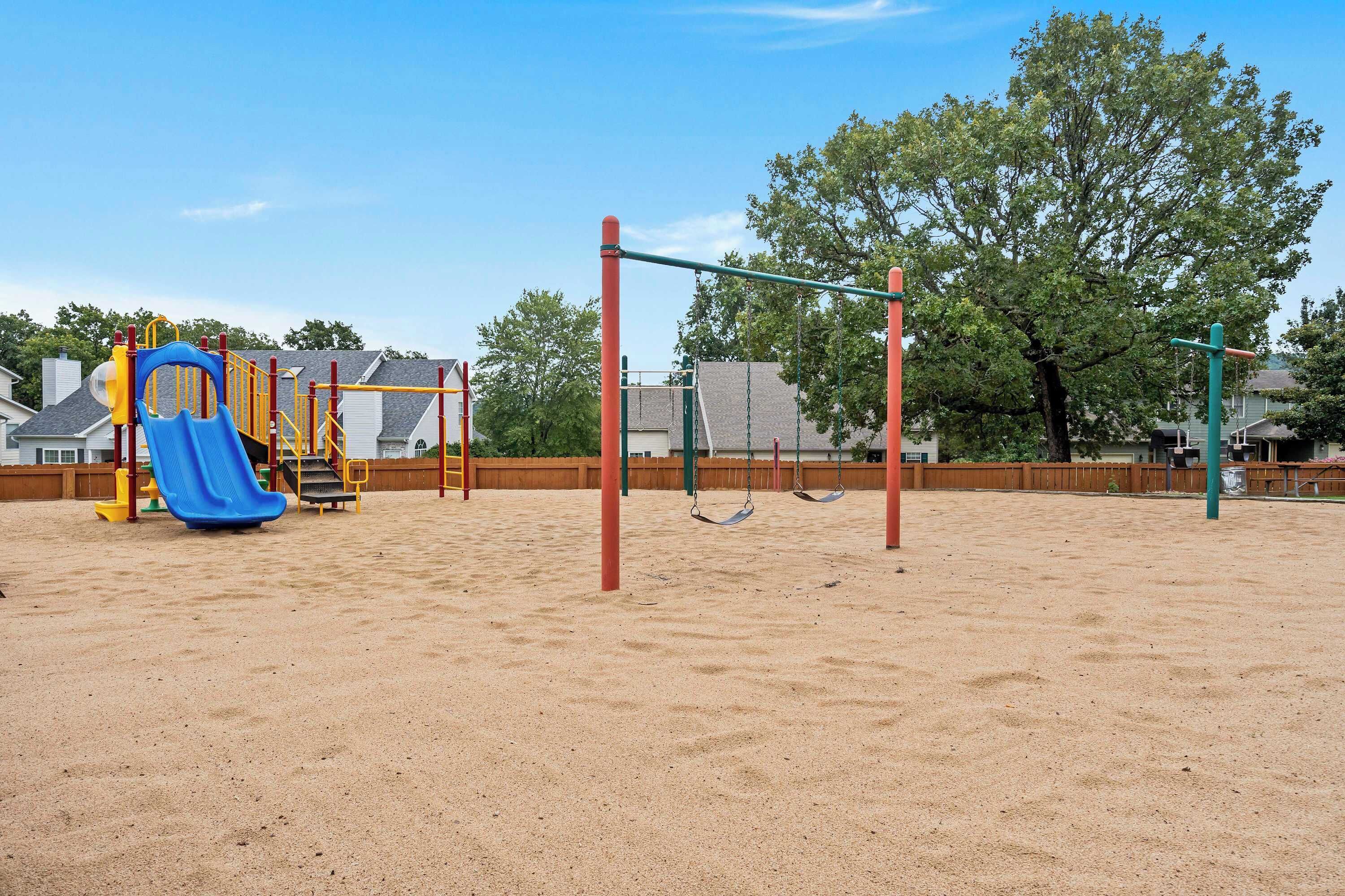 A playground with a blue slide, swings, and sand.