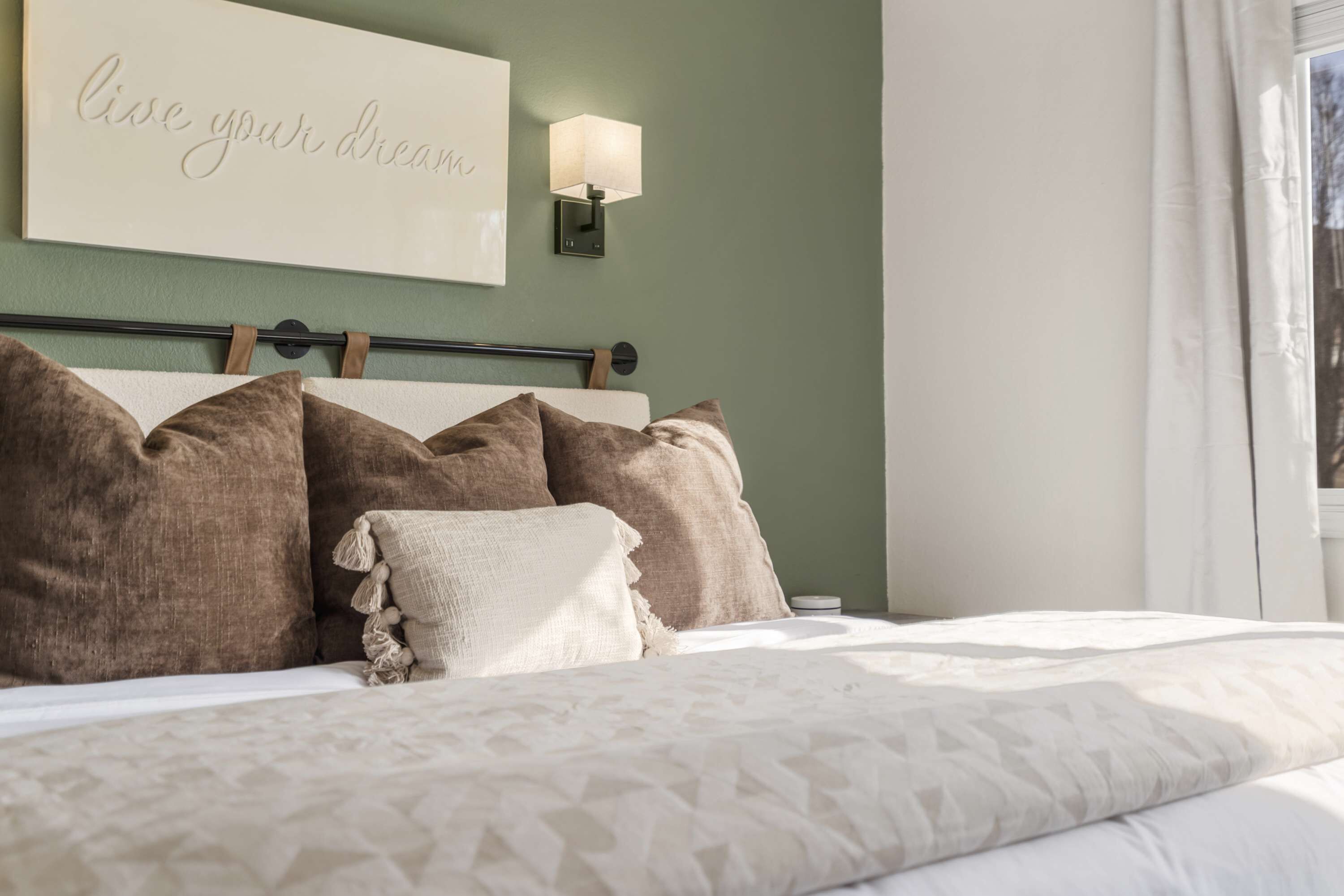 A neatly made bed with a patterned bedspread, a headboard with a motivational quote, and a bedside lamp.