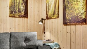 Een kamer met houten lambrisering, een grijze bank, een leeslamp en twee wanddecoraties met een bosmotief.