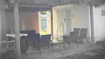 Un área de estar al aire libre techada con mesa y sillas, una parrilla y un techo de paja.